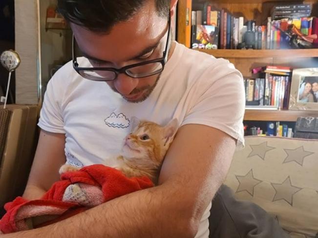 Man looks down at an orange tabby cat he's holding in his arms